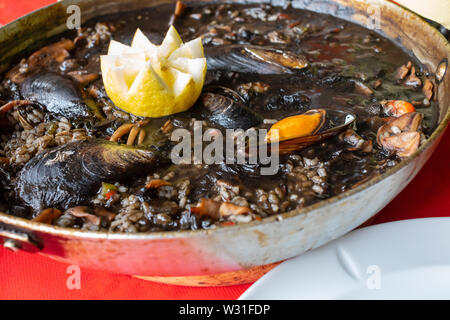 Close-up de riz noir avec squid -à l'encre- moules, palourdes et autres fruits de mer. Présenté en paellera. Banque D'Images