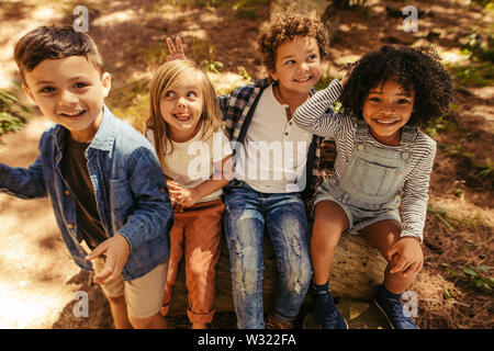 Groupe de quatre enfants assis sur un journal en bois et d'avoir du plaisir. Groupe multi-ethnique des enfants jouant dans un parc. Banque D'Images