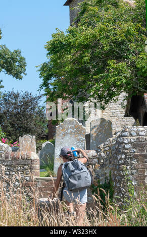 Walker sur le sentier public en utilisant les marches en pierre étouffe pour traverser sur le mur de pierre de la St Pierre et de l'église St Paul, West Wittering, Royaume-Uni Banque D'Images