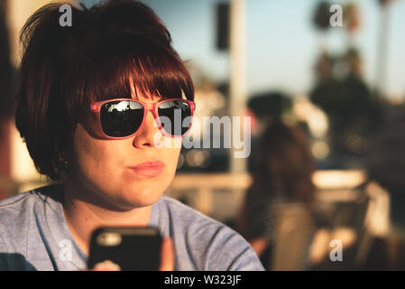 LA, USA - 31 octobre 2018 : Tête Portrait de femme caucasienne dans lunettes funky regarde Hollywood Blvd, LA pendant un coucher de soleil lumineux Banque D'Images