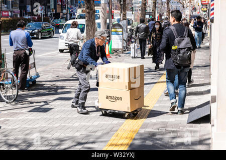 Tokyo, Japon - 4 Avril, 2019 : old man poussant Dolly, la livraison des paquets dans des boîtes d'Amazon sur le trottoir de la rue de Shinjuku Banque D'Images