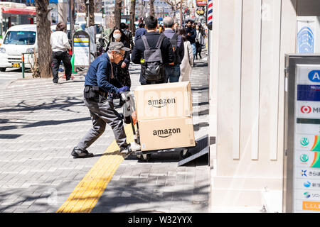 Tokyo, Japon - 4 Avril, 2019 : old man worker dolly, poussant la livraison des paquets dans des boîtes d'Amazon sur le trottoir de la rue de Shinjuku Banque D'Images