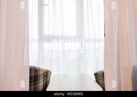 Deux fauteuils et une petite table basse dans la nouvelle maison sur balcon couvert dans l'organisation d'accueil du modèle ou d'un appartement avec vue à travers les stores rideaux blancs Banque D'Images