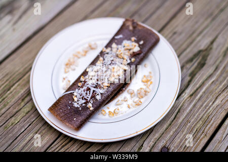 Libre de chocolat banane dessert vegan crêpe wrap avec du riz chips, flocons de noix de coco faite en bouteille sur table en bois plaque de Banque D'Images
