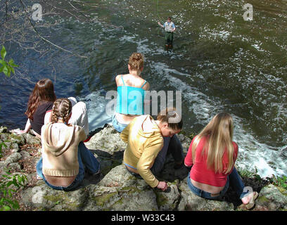 2229, CT USA. Mai 2016. Les jeunes femmes de penser et assis sur une falaise à regarder vers le bas un pêcheur en action. Banque D'Images