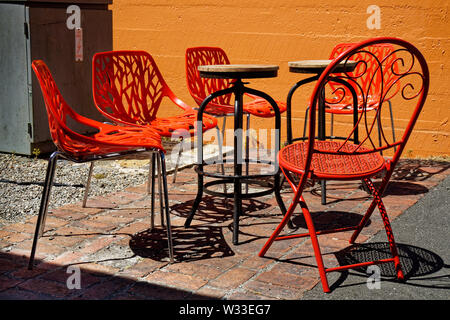Chaises empilables, rouge vif et réduite, et de tables en bois dans un café jardin, Nouvelle-Zélande. Banque D'Images