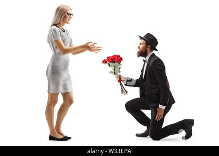 Profil de pleine longueur tourné d'un homme barbu à genoux et donner un bouquet de roses rouges à une femme isolée sur fond blanc Banque D'Images
