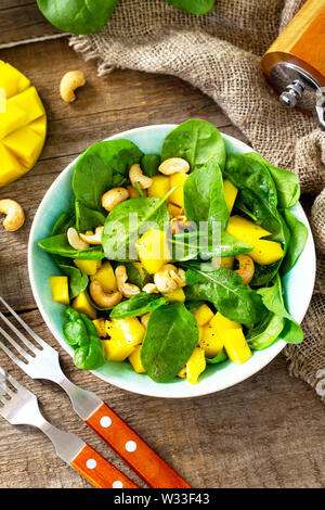 Menu de régime, la nourriture végétalienne. Salade saine avec des épinards, de la mangue, vinaigrette aux noix et sur une table en bois rustique. Banque D'Images
