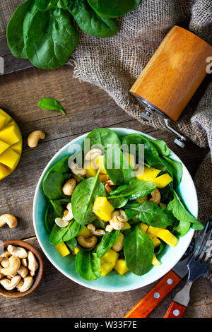 Menu de régime, la nourriture végétalienne. Salade saine avec des épinards, de la mangue, vinaigrette aux noix et sur une table en bois rustique. Vue supérieure de la télévision. Banque D'Images