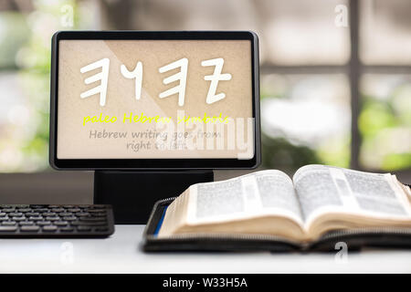 Une tablette montrant les paléo hébreu symboles pour le nom de Dieu sur un bureau avec un clavier, a ouvert la sainte bible et en arrière-plan. Banque D'Images