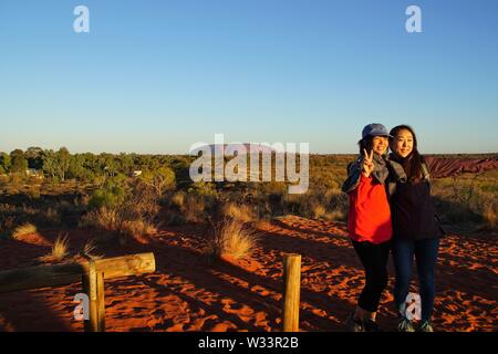 Fin d'après-midi l'éclairage de deux jeunes femmes qui pose pour une photographie à Uluru dans l'arrière-plan Banque D'Images