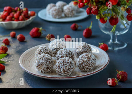 Boules de pâte à la noix de coco, fraises et copeaux de chocolat situé sur un fond sombre, photo horizontale Banque D'Images