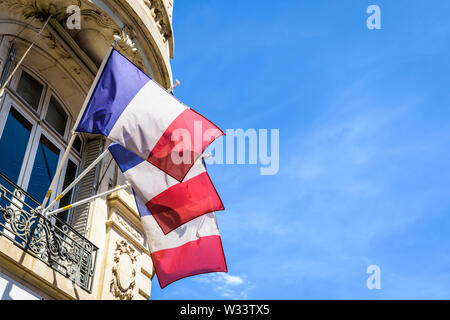 Low angle view of trois drapeaux français de terrasse un immeuble haussmannien à Paris, en France, sur une journée ensoleillée. Banque D'Images