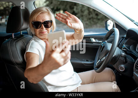 Senior Business Woman talking with smart phone en conduisant une voiture. Concept d'une population active au cours de l'âge de la retraite Banque D'Images