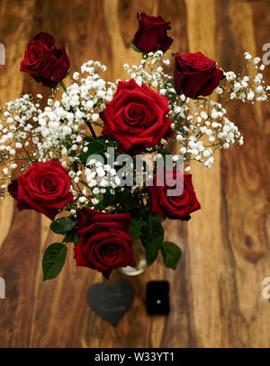 Groupe de sept belles roses rouges avec bague de fiançailles et pierre gravée en forme de coeur debout sur une table en bois Banque D'Images