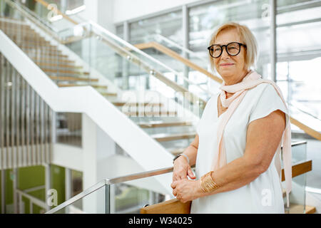 Portrait d'un certain senior woman dressed in white shirt debout sur l'escalier de l'édifice moderne Banque D'Images