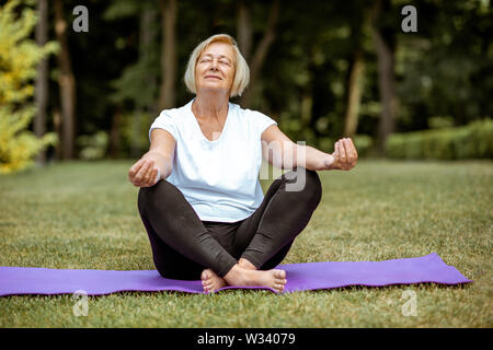 Portrait of a senior woman sitting on le tapis de yoga, faire du sport dans le parc. Concept d'une vie active à la retraite Banque D'Images
