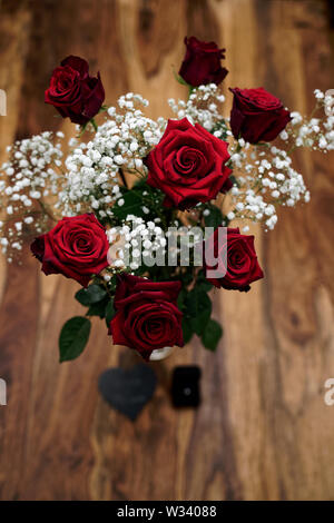 Groupe de sept belles roses rouges avec bague de fiançailles et pierre gravée en forme de coeur debout sur une table en bois Banque D'Images