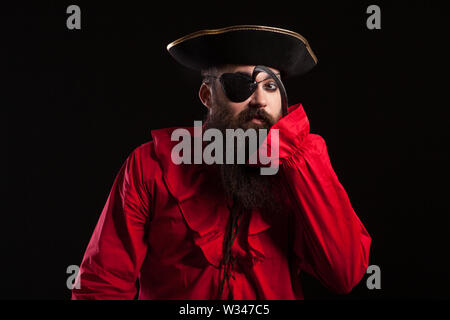 Homme barbu attrayant dans un costume de pirate pour le carnaval de toucher son œil avec son crochet du bras. L'homme dans un costume d'halloween. Banque D'Images