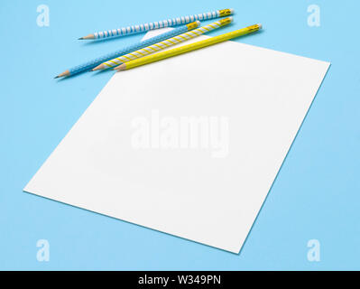 Feuille de papier, crayons à rayures bleu et jaune sur fond bleu pastel. Banque D'Images