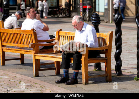 Tayside, Dundee, Ecosse, Royaume-Uni. 12 juillet, 2019. Météo France : Un homme âgé assis sur le siège d'été de la lecture du journal Courier à Dundee, Royaume-Uni Banque D'Images