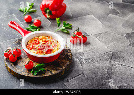 Frittata aux poivrons, tomates et le salami dans la poêle en céramique. Genre d'omelette italienne aux légumes. Banque D'Images