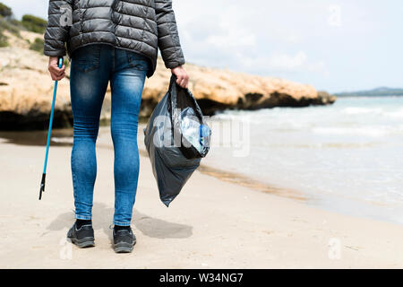 Libre d'un homme de race blanche, vu de derrière, la collecte des déchets avec une portée extender, sur une plage solitaire, comme une action pour nettoyer l'environne naturelles Banque D'Images