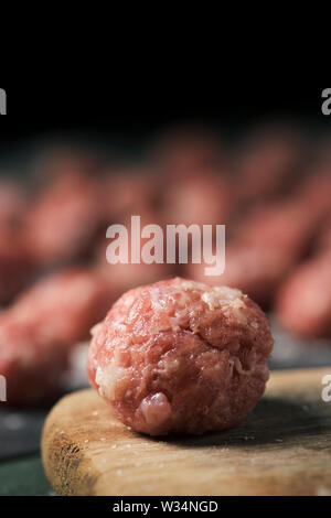 Libre d'une matière première meatball sur une planche à découper en bois placé sur une table et quelques autres des boulettes de viande dans l'arrière-plan Banque D'Images