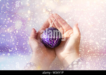 Les paillettes brillantes sur une boule de Noël. Closeup of a young girl's hands holding une boule de noël. Banque D'Images