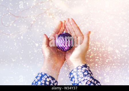 Les paillettes brillantes sur une boule de Noël. Closeup of a young girl's hands holding une boule de noël. Banque D'Images