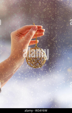 Concept de Noël avec la main et Golden Ball - jouet d'arbre de Noël. Décoration de Noël sur fond de neige. Close-up Banque D'Images