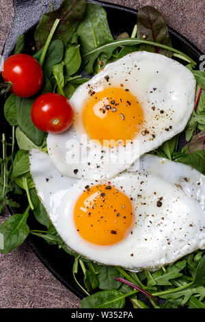 Close up de jaunes d'oeufs au plat avec des épinards et salade de roquette et de tomates cerises et de poivre. Concept de petit-déjeuner anglais. Vue d'en haut Banque D'Images