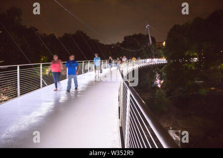 GREENVILLE, SC (USA) - 5 juillet 2019 : les piétons traverser le pont de la Liberté illuminée dans la nuit du parc des chutes. Banque D'Images