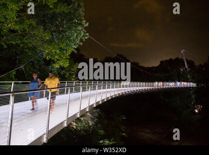 GREENVILLE, SC (USA) - 5 juillet 2019 : les piétons traverser le pont de la Liberté illuminée dans la nuit du parc des chutes. Banque D'Images