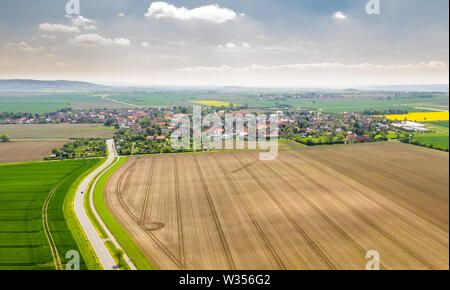 Vue aérienne d'une route entre les champs marqués d'un village et d'un ciel dramatique avec des nuages en arrière-plan. Banque D'Images