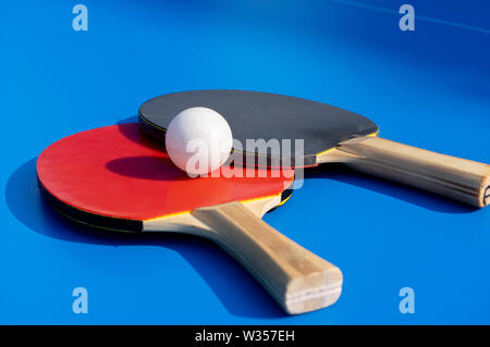 Gros plan de deux palettes de tennis de table avec une balle sur la table bleu Banque D'Images