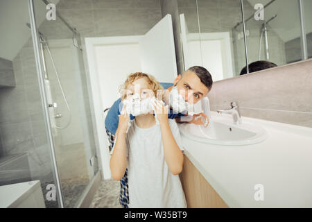 Vrai homme. Garçon agréable d'appliquer la mousse à raser sur son visage tout en voulant apprendre comment se raser Banque D'Images