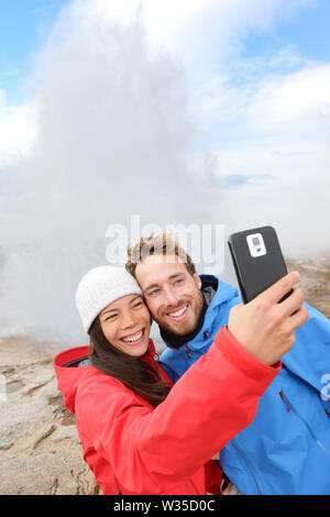 Les touristes l'Islande photo de selfies Strokkur geyser. Couple heureux de visiter de célèbres attractions touristiques, monuments et sur le cercle d'or. Voyage multiraciale en vacances locations de tourisme. Banque D'Images