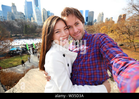 Dating jeune couple heureux en amour taking self-portrait photo selfies dans Central Park, New York City à la fin de l'automne au début de l'hiver avec patinoire en arrière-plan. Les touristes s'amuser ce jour, Manhattan, USA. Banque D'Images