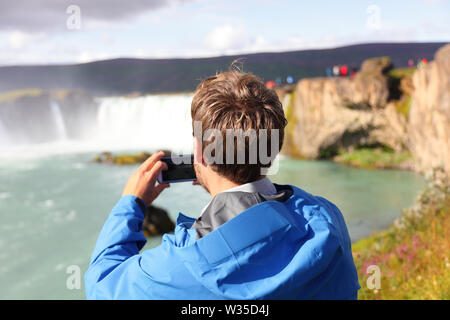 Photo prise touristiques avec le smartphone de Godafoss cascade sur l'Islande. Man taking picture with smart phone caméra sur billet visiter les attractions touristiques et monuments de la nature islandaise sur Ring Road. Banque D'Images