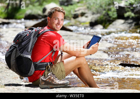 Ordinateur tablette homme hiker relaxing by river holding ebook reader lire livre ou site, randonnées dans le parc Yosemite, USA en utilisant app voyage ou carte pendant la randonnée. Banque D'Images