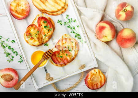 Petit-déjeuner gastronomique de l'été - sandwichs (pain grillé, bruschetta) avec les pêches grillées, fromage à la crème (ricotta, mascarpone), le thym et le miel sur un vieux wh Banque D'Images