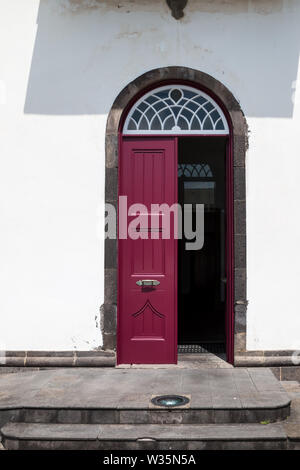 La moitié a ouvert ses portes en bois bourgogne porte d'une maison traditionnelle lumineuse avec façade blanche. Caillebotis blanc et un arc sur le dessus. Povoacao, Sao Miguel, Açores est Banque D'Images