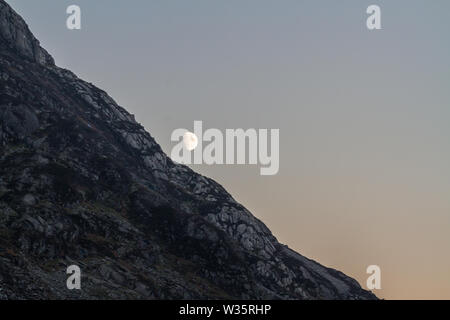 Près de pleine lune qui s'élève au-dessus de falaise dans la région de Snowdonia, Banque D'Images