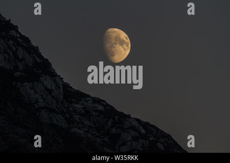 Près de pleine lune qui s'élève au-dessus de falaise dans la région de Snowdonia, vue au téléobjectif Banque D'Images