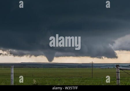 Une grande tornade cône sous la base d'une sombre tempête sur les plaines du Wyoming, avec une clôture en fil barbelé au premier plan. Banque D'Images