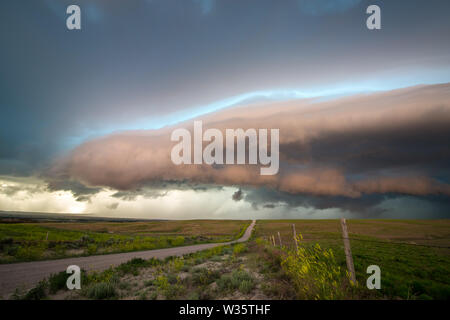 Un chemin de terre dans la campagne mène à la plate-forme de cloud d'une violente tempête dans la lumière du soir. Banque D'Images