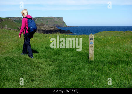 Woman Walking in Dunseverick Harbour avec Benbane Head en arrière-plan sur le Giant's Causeway chemin côtier, comté d'Antrim, en Irlande du Nord, Royaume-Uni Banque D'Images