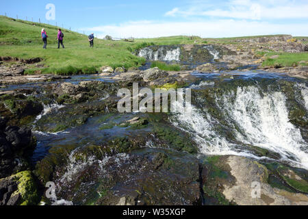 Trois personnes marchant par des chutes d'eau près de Dunseverick Harbour/Château sur le Giant's Causeway chemin côtier, comté d'Antrim, en Irlande du Nord, Royaume-Uni. Banque D'Images