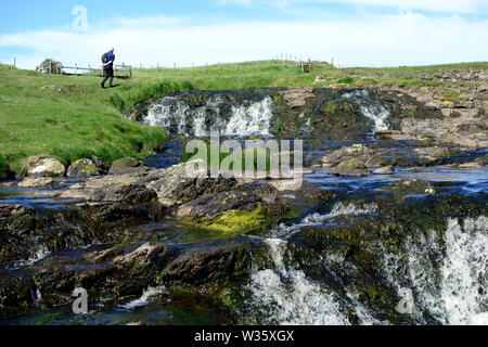 Homme marchant par des chutes d'eau près de Dunseverick Harbour/Château sur le Giant's Causeway chemin côtier, comté d'Antrim, en Irlande du Nord, Royaume-Uni. Banque D'Images